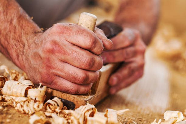 Mains du menuisier au rabot, copeaux de bois dans l'atelier